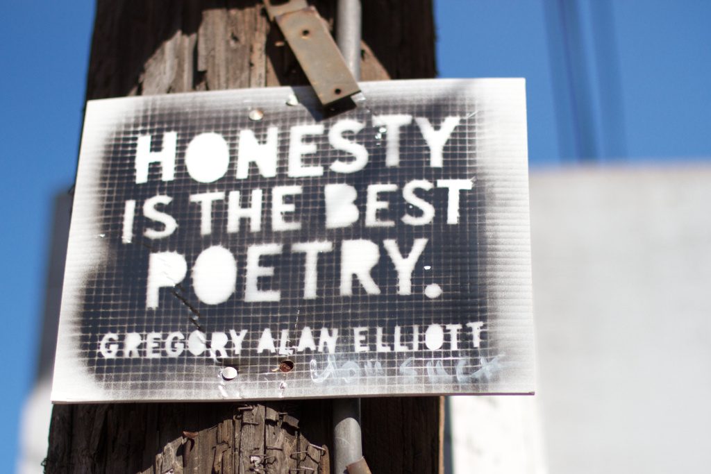 photo of a sign on a telephone post: black spray paint over stenciled lettering: HONESTY IS THE BEST POETRY - GREGORY ALAN ELLIOT